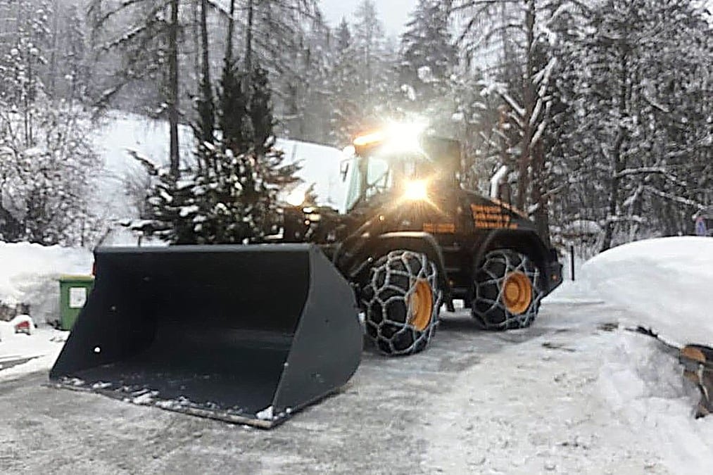 Traktor mit Schneepflug beim Räumen eines verschneiten Güterwegs im Pongau